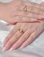 Close-up of hands with pink nail polish wearing gold rings on a light background