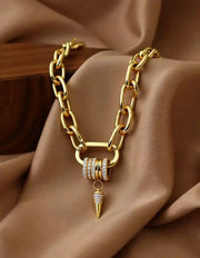 Chunky gold chain necklace with spike pendant on beige fabric