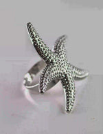 Silver starfish-shaped ring on a light gray background
