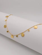 Dainty gold necklace with hammered coins and zircon drops on white background