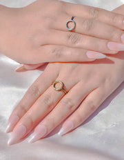 Close-up of hands with pink nail polish wearing gold rings on a light background