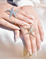 Two hands wearing starfish-shaped rings on a soft background